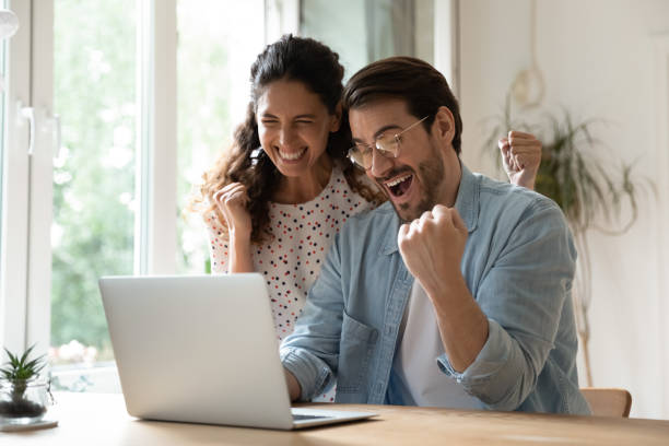 Excited Caucasian couple overjoyed with online deal on laptop Overjoyed millennial man and woman triumph win online lottery on laptop. Happy excited young Caucasian couple feel euphoric with good email, get amazing sale offer or discount deal on computer. unusual couple stock pictures, royalty-free photos & images