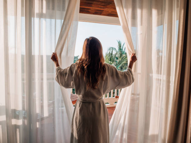 mujer abriendo cortinas en la habitación al amanecer - albornoz fotografías e imágenes de stock