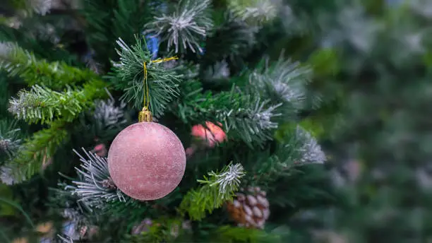 Photo of Christmas tree with a delicate pink ball with snowflakes. Festive Christmas blurred background design. Winter seasonal holiday, christmas decoration