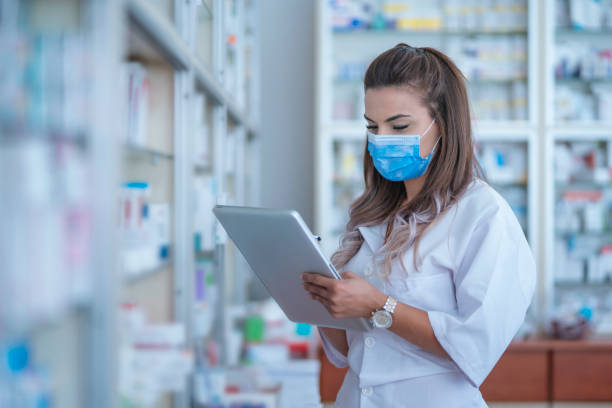 Female pharmacist with digital tablet wearing a medical mask is checking the prescription Female pharmacist with digital tablet wearing a medical mask pharmacy tech stock pictures, royalty-free photos & images