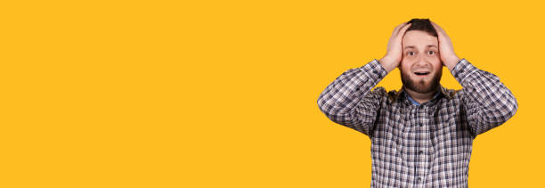 istock Man with beard holding his head with hand, panic, isolated on orange background, copy space template, banner. 1277626639