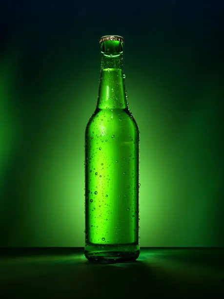 Photo of Single green beer bottle with water drops against green illuminated background.