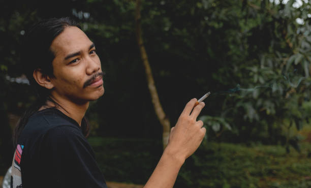 istock A long-haired Asian man with a beard holding a cigarette standing outside 1277633007