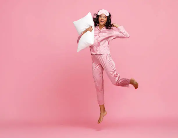Photo of Excited woman in pajama jumping with pillow