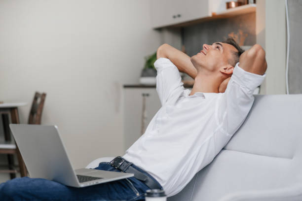 istock dreaming young man with a laptop sitting on the couch 1277635059