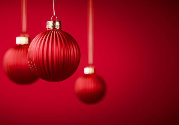 Group of three red vertically striped Christmas balls. Baubles hanging on strings against burgundy red background. Christmas decoration, festive atmosphere concept. Selective focus, copy space.