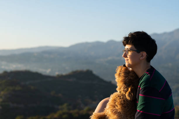 Non-binary woman holding her miniature golden doodle puppy out in nature.