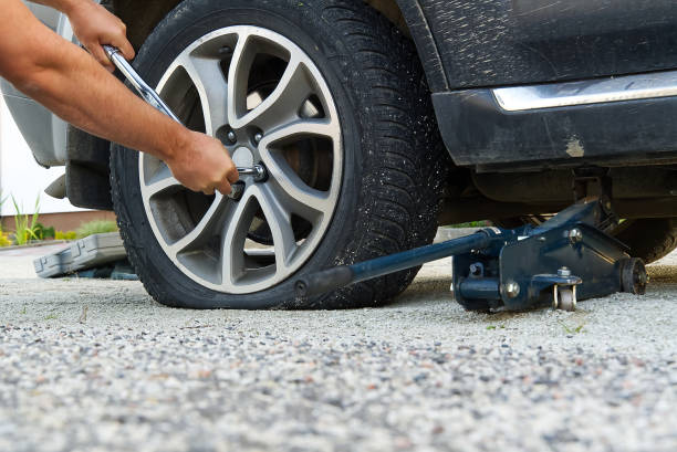 istock Man changing wheel. tire changer changing flat car tire. Help on road concept. Mechanic hands unscrews a flat tire of a car raised on a jack 1277647802