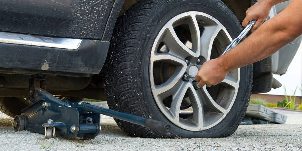 istock Man changing wheel. tire changer changing flat car tire. Help on road concept. Mechanic hands unscrews a flat tire of a car raised on a jack 1277648278