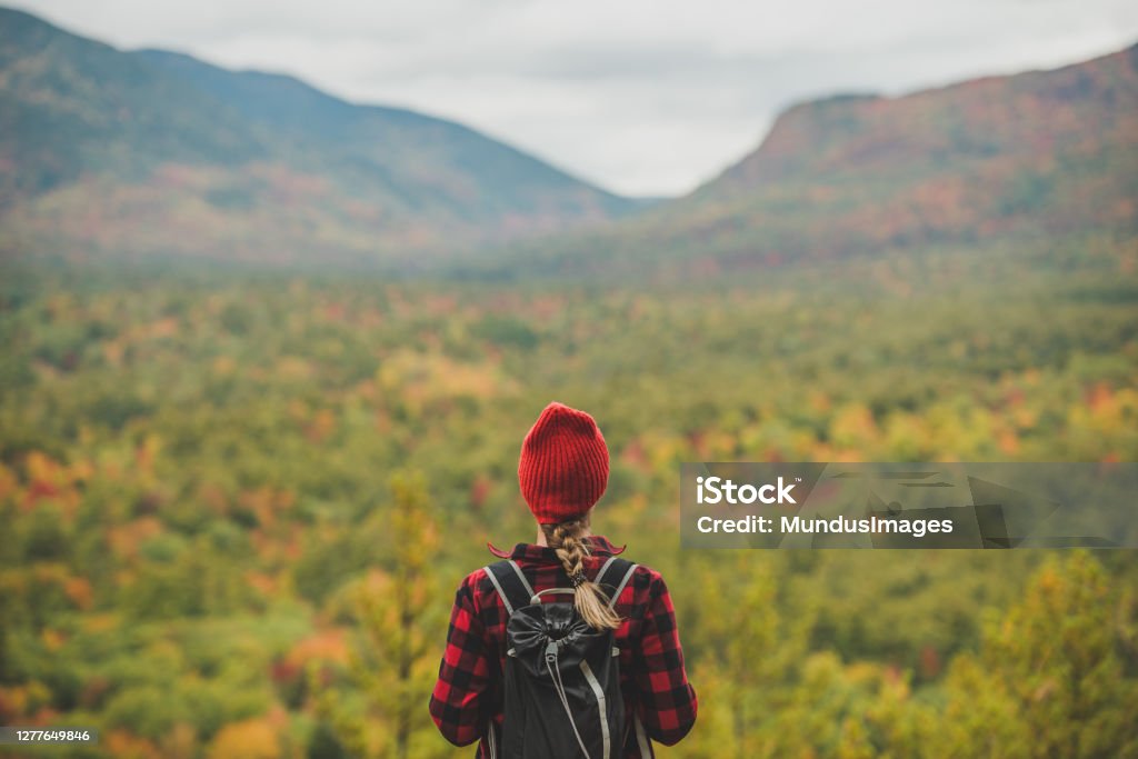 Female hiker surrounded by beautiful fall colors Female hiker in the mountains on a fall day with vibrant fall trees. Hiking Stock Photo