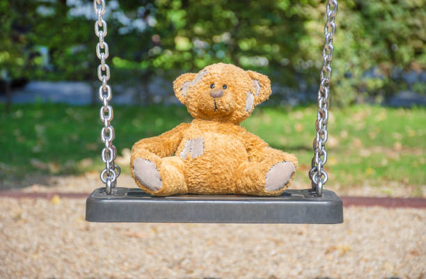 istock Cute little teddy bear standing alone on a swing in empty park on a beautiful sunny day. 1277656102