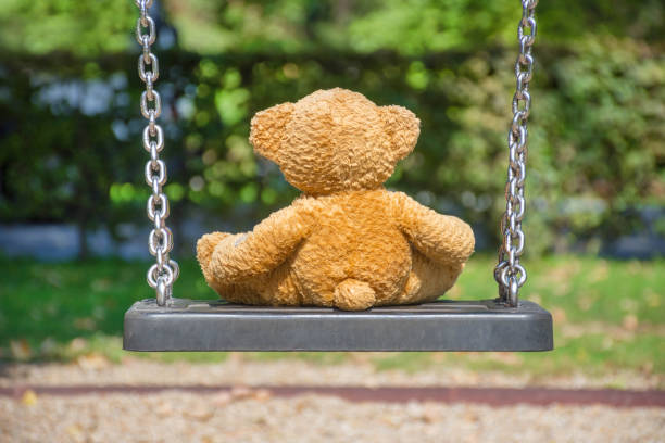 istock Cute little teddy bear standing alone on a swing in empty park on a beautiful sunny day. 1277656110