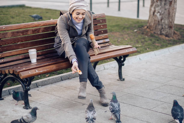 Young woman sitting on the bench and feeding a birds