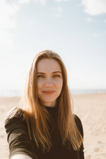 긴 머리와 예쁜 여성의 초상화, 금발은 모래 해변에서 휴대 전화에 셀카를 찍습니다. - 셀카 뉴스 사진 이미지