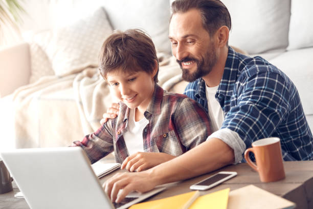 istock Father and son at home sitting at table playing game on laptop smiling happy 1277659429