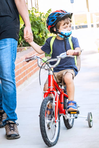 istock Man walking his son back to school, boy is riding his bicycle both wearing protective face masks 1277664451