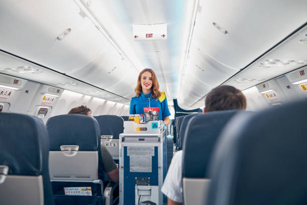 Air stewardess serving food on the board commercial airplane Interior of international airplane with passengers on seats and stewardess in uniform walking the aisle crew stock pictures, royalty-free photos & images