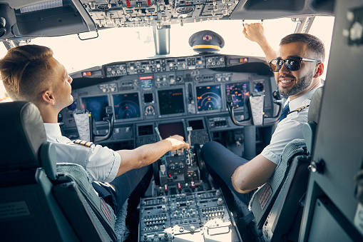 Back view portrait of two pilot in uniform working while one man in sunglasses looking at the photo camera