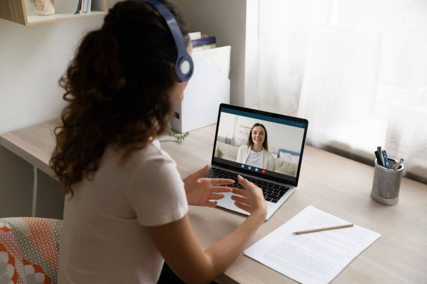 Female student in headphones talk on video call with teacher Top back view of female student in headphones sit at desk at home talk on video call with teacher or trainer. Woman in earphones have webcam conference, study distant on computer. Education concept. online tutors stock pictures, royalty-free photos & images