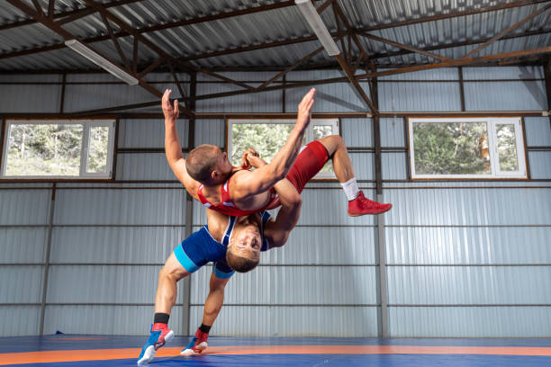 Two young sportsmens Two young sportsmens wrestlers in red and blue uniform wrestling against wrestling carpet, view side wrestling stock pictures, royalty-free photos & images