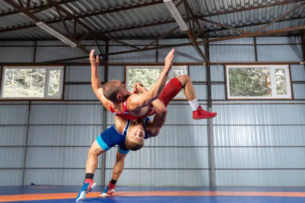 Two young sportsmens wrestlers in red and blue uniform wrestling against wrestling carpet, view side