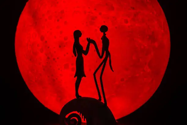 Photo of The silhouette of Halloween Ghost couple decorations.There's a red full moon in the background. Halloween horror concept.