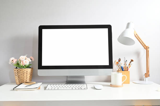 istock Mock up image of computer pc with white screen, coffee cup, plant, lamp and office supplies on minimal work desk. 1277705010