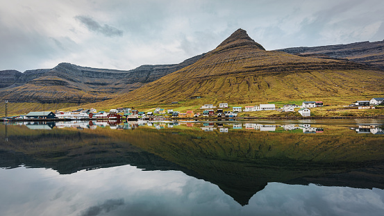 Norðdepil - Norddeble Town Panorama mirroring in the North Atlantic Ocean under cloudy skyscape. View to the coastal town and houses of Norddeble under green faroese mountain range at the North Atlantic Ocean Fjord. Norðdepil - Norddeble Town, Klaksvík, East Coast of Borðoy Island, between Bordoy Island and Viðoy - Vidoy Island, Faroe Islands, Kingdom of Denmark, Nordic Countries, Scandinavia, Europe