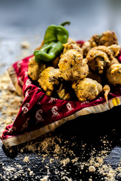 istock Close up shot of freshly fried methi pakora in a container on a black surface along with some spices and a chickpea flour spread on the surface. Methi pakora in a serving dish on the black surface. 1277720997