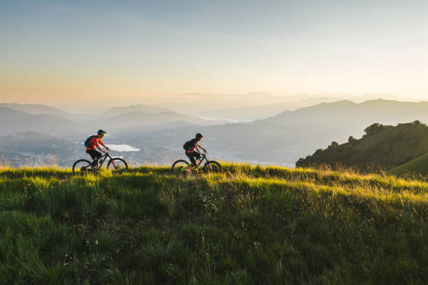 Mountain bikers ride along grassy mountain ridge Dolomites illuminated in the background dolomites photos stock pictures, royalty-free photos & images