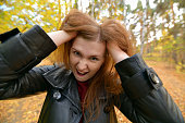 Portrait of crazy screaming young woman. The red-haired girl with her mouth open and screams. Screaming angry  girl took her head in her hands.