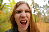 Portrait of crazy screaming young woman. The red-haired girl with her mouth open and screams. Emotional girl. Angry girl looking at camera.