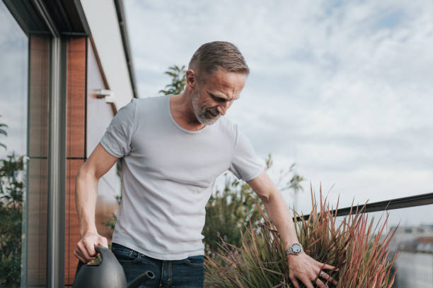 istock handsome bearded midaged man pouring plants at balcony 1277733060