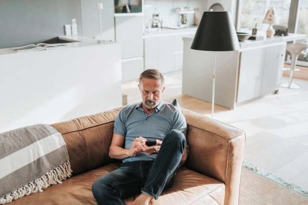 istock handsome bearded midaged man looking at mobile phone on sofa 1277733098