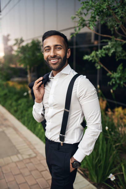 Handsome dapper bearded smiling Indian businessman standing with jacket over shoulder