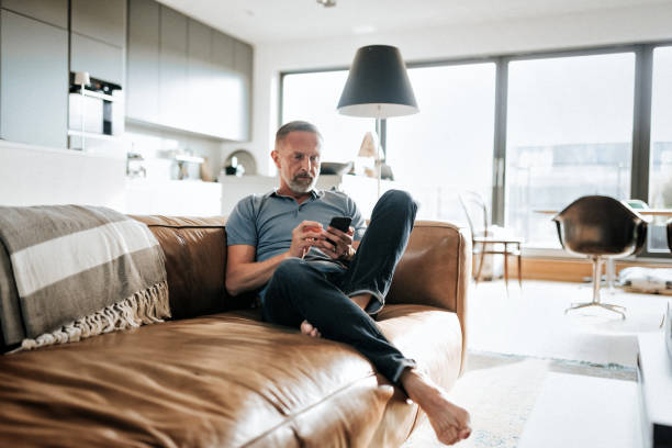 handsome bearded midaged man looking at mobile phone on sofa handsome  bearded mid aged man looking at mobile on sofa central berlin photos stock pictures, royalty-free photos & images