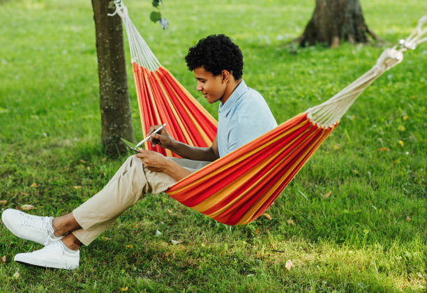 istock Young man sitting on hammock in the park and drawing on digital tablet 1277737340