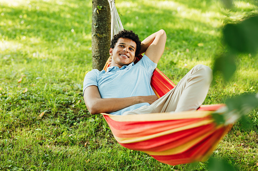 Young smiling guy with hand behind head relaxing in hammock
