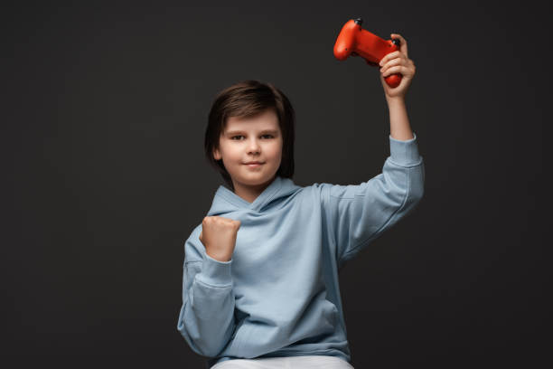 ritratto di ragazzo carino di 10-12 anni in piedi con joystick in mano che gioca e guarda la macchina fotografica. concetto di infanzia - 10 11 years cheerful happiness fun foto e immagini stock