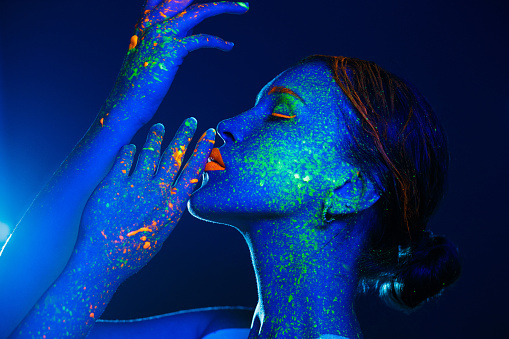 Creative portrait of young woman's portrait painted with fluorescent makeup that glowing under the ultraviolet light.