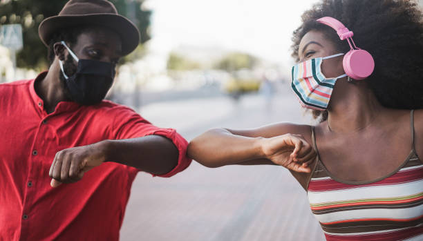 African people wearing face masks while bumping their elbows instead of greetings with hugs - Social distance between friends concept - Focus on woman's eye African people wearing face masks while bumping their elbows instead of greetings with hugs - Social distance between friends concept - Focus on woman's eye elbow photos stock pictures, royalty-free photos & images