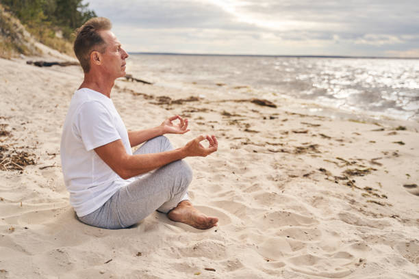 istock Mature man meditating in morning in beach 1277754025