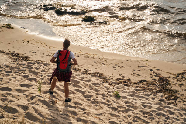 Top view of mature male carrying rucksack while going hiking in beach near wavy shore