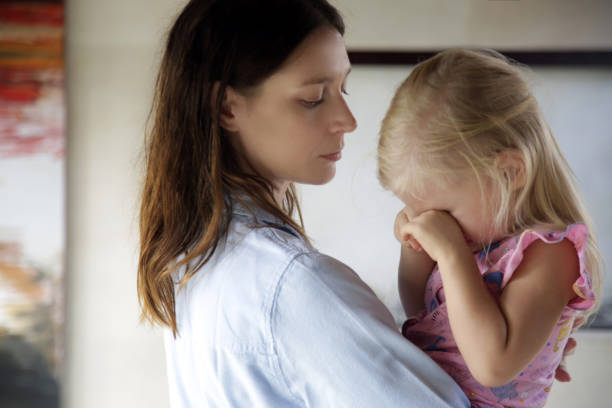 giovane madre che abbraccia la figlia piccola che piange. figlia triste tra le braccia di sua madre. - pensive only baby girls baby girls baby foto e immagini stock