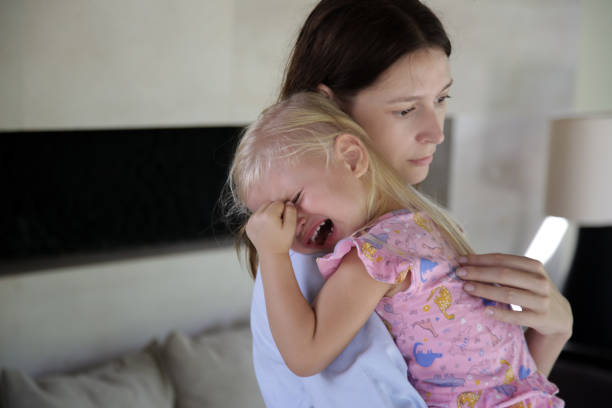 giovane madre che abbraccia la figlia piccola che piange. figlia triste tra le braccia di sua madre. - women crying distraught thinking foto e immagini stock