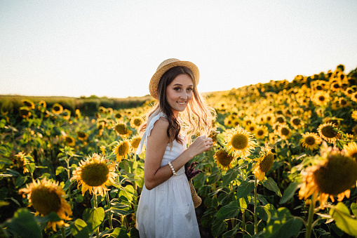 Young happy woman in Provence dress code  is walking in the sunflower field at the sunset