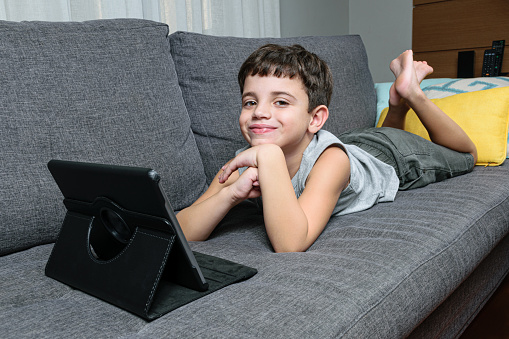 7 year old child sitting on the couch and interacting with the tablet.