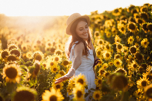 Young happy woman in Provence dress code  is walking in the sunflower field at the sunset