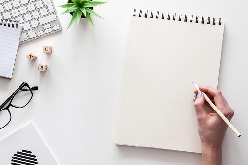 White office desk with mockup. Keyboard, notebook, glasses and succulent. View from above. Hand with a pencil.