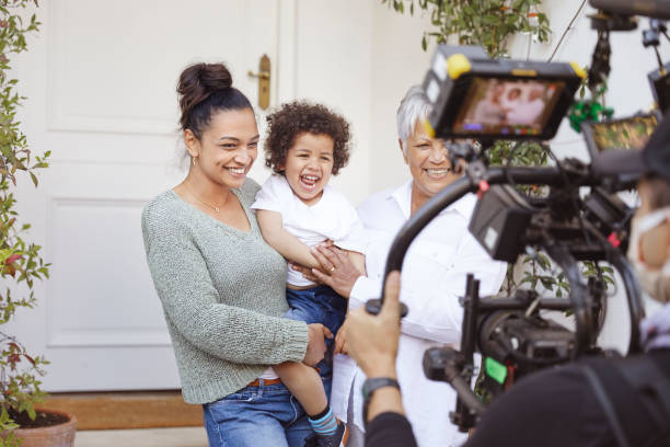 Happy multigeneration family Portrait of happy mother holding her son together with grandma and being filmed by professional videographer holding camera on easy rig. media interview photos stock pictures, royalty-free photos & images